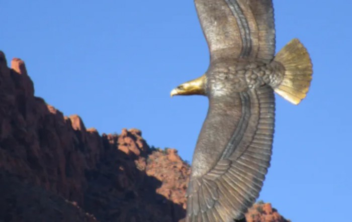 An eagle soaring in the clear blue sky above rugged mountains.
