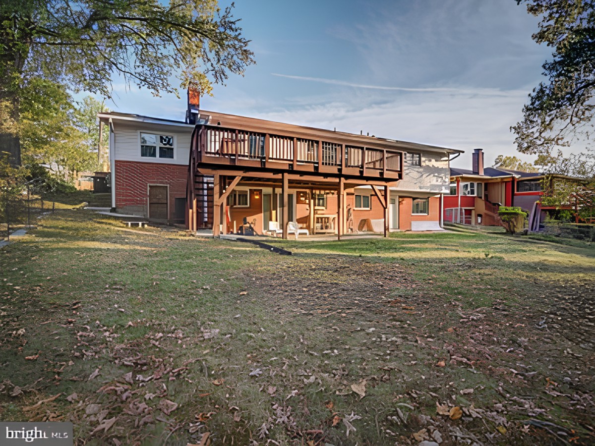A spacious backyard of a two-story residential house with a large lawn and surrounding trees.