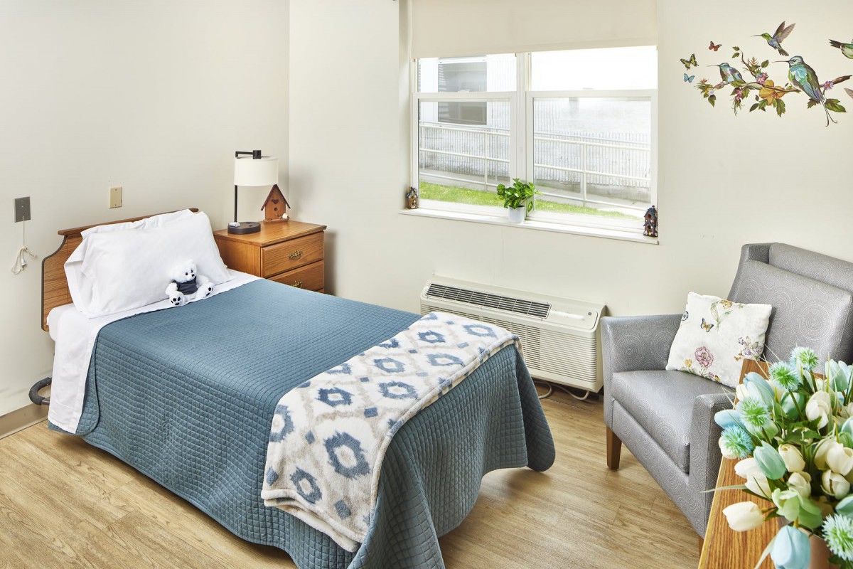 A modern bedroom with a neatly made bed, wooden nightstand, and comfortable armchair by the window.