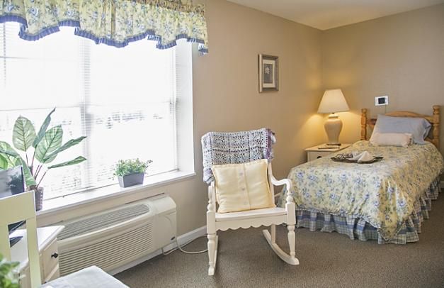 A cozy bedroom with a rocking chair near a window, showcasing soft lighting and decorative elements.