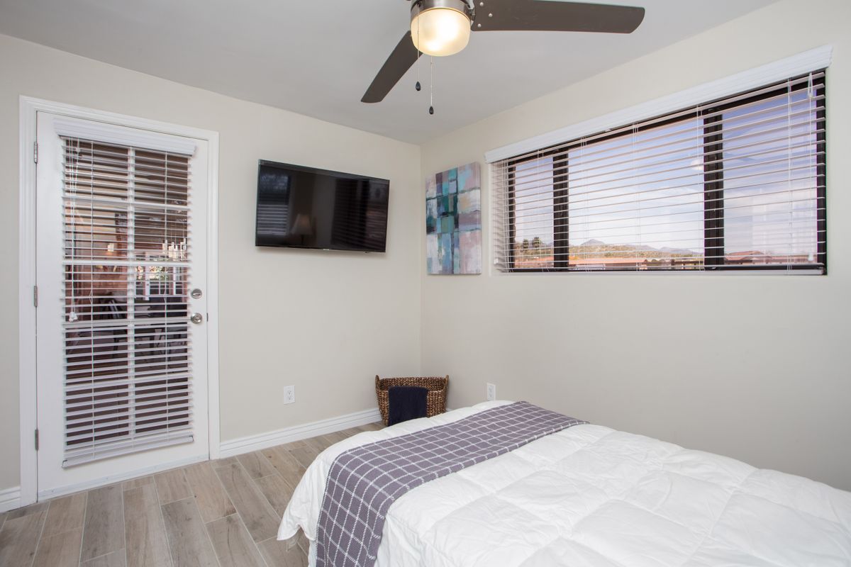 A modern minimalist bedroom with a ceiling fan, wall-mounted television, and window blinds.