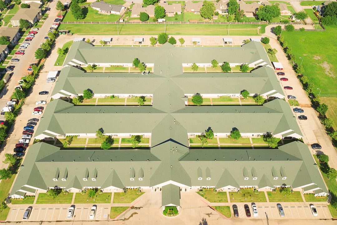 Aerial view of a large building complex with a green roof and surrounding parking areas.
