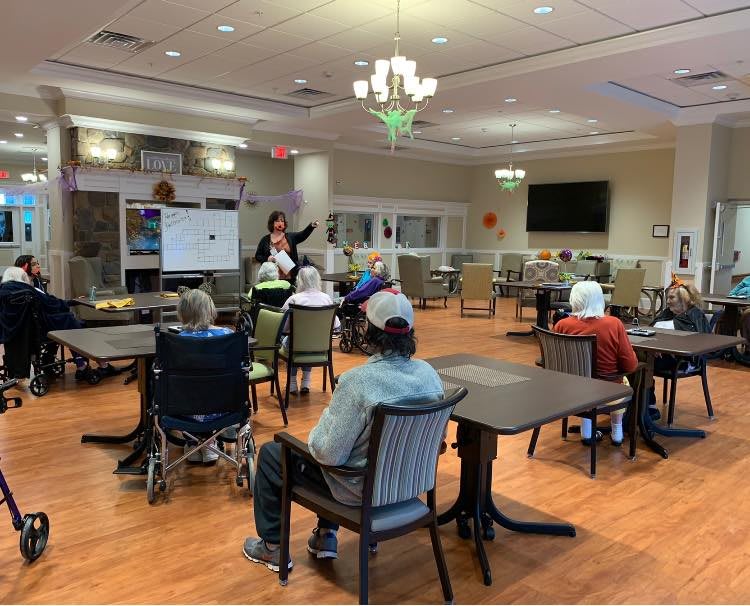 A group of seniors attending a presentation in a nursing home setting.