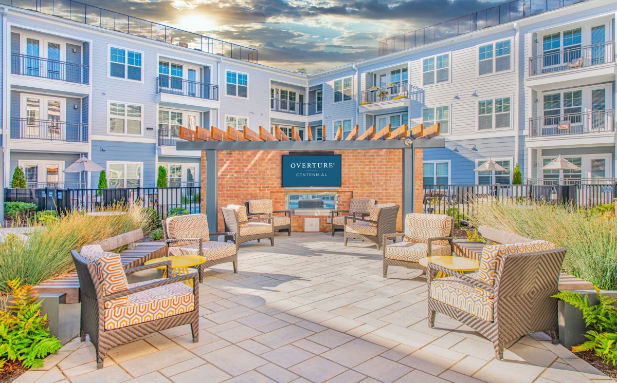 A modern outdoor patio with comfortable seating and a fireplace, situated within an apartment complex.
