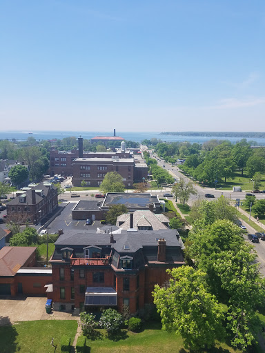 A panoramic view of a city overlooking a waterfront, featuring lush greenery and a clear blue sky.