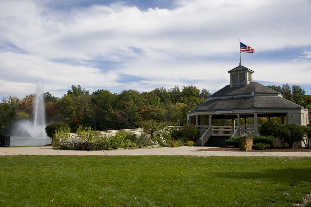A scenic view of a park with a gazebo and an American flag under a partly cloudy sky.