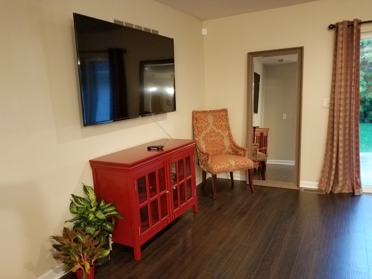 A cozy living room with a mounted television, red cabinet, armchair, and a large mirror.