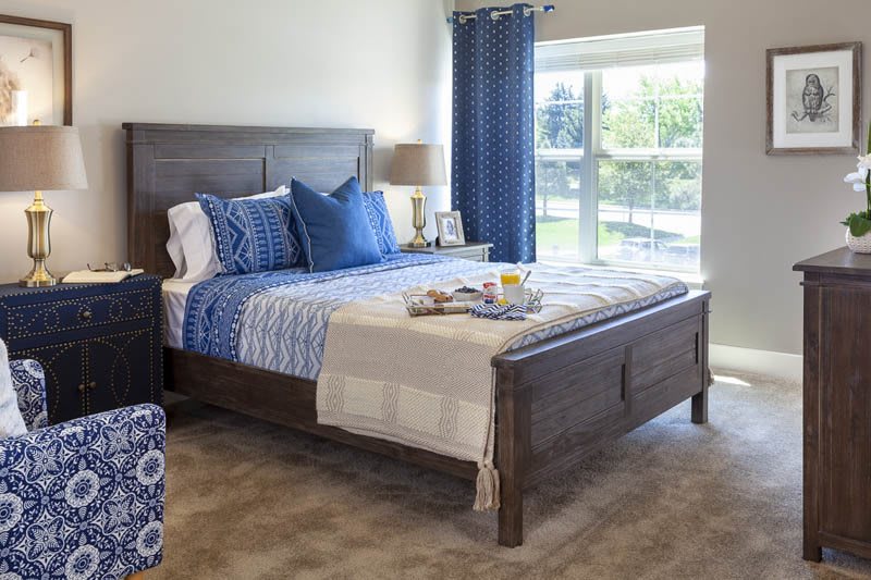 A cozy bedroom featuring a large bed with blue accents and a window with curtains.