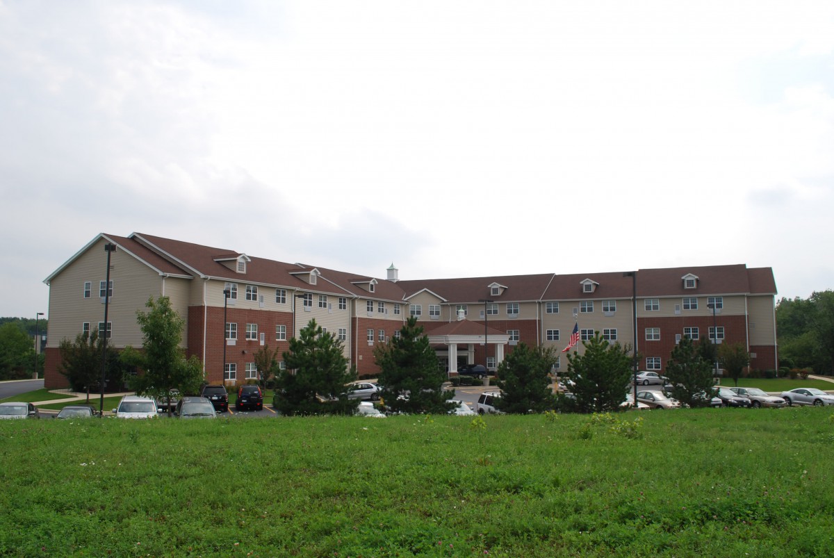 A large hospital building with a parking lot and surrounding greenery under a cloudy sky.