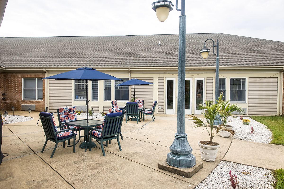 A peaceful outdoor patio area with tables, chairs, and umbrellas surrounded by lamp posts and potted plants.