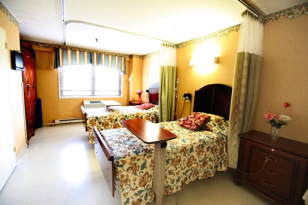 A hospital room with two neatly made beds separated by privacy curtains.