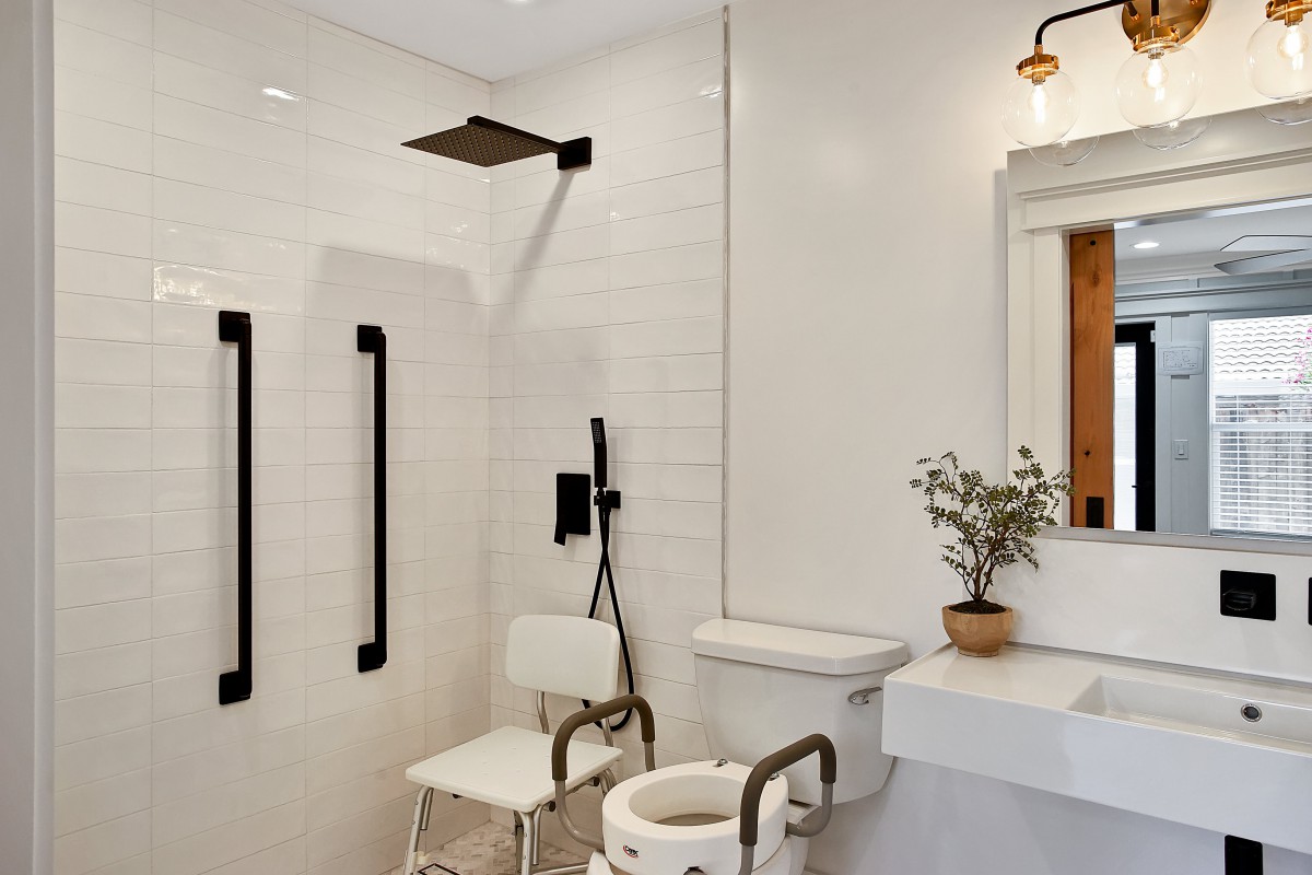 An accessible bathroom with a modern design, featuring a shower, grab bars, a chair, and a sink.