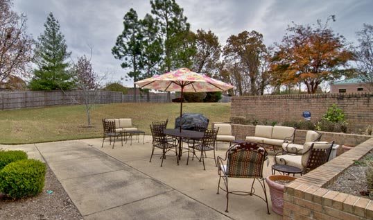 A spacious outdoor patio with seating and a large umbrella, surrounded by trees.