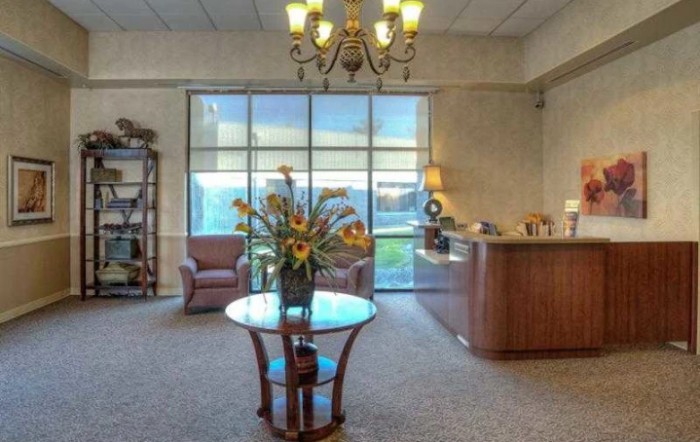 A welcoming office lobby featuring a glass table with flowers, comfortable armchairs, and a reception desk under an elegant chandelier.