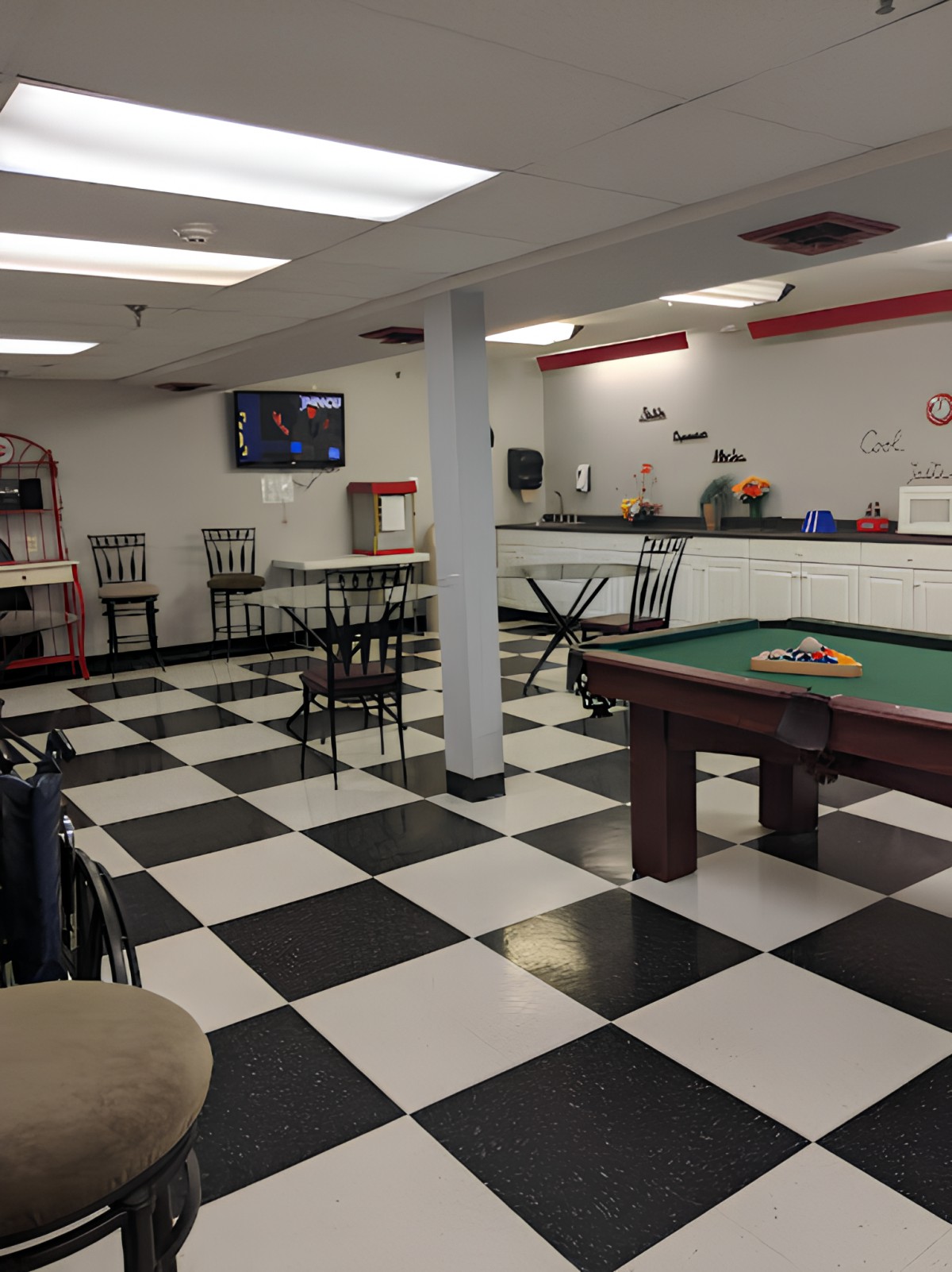 A game room with a checkered floor, featuring a pool table and cafe-style seating.