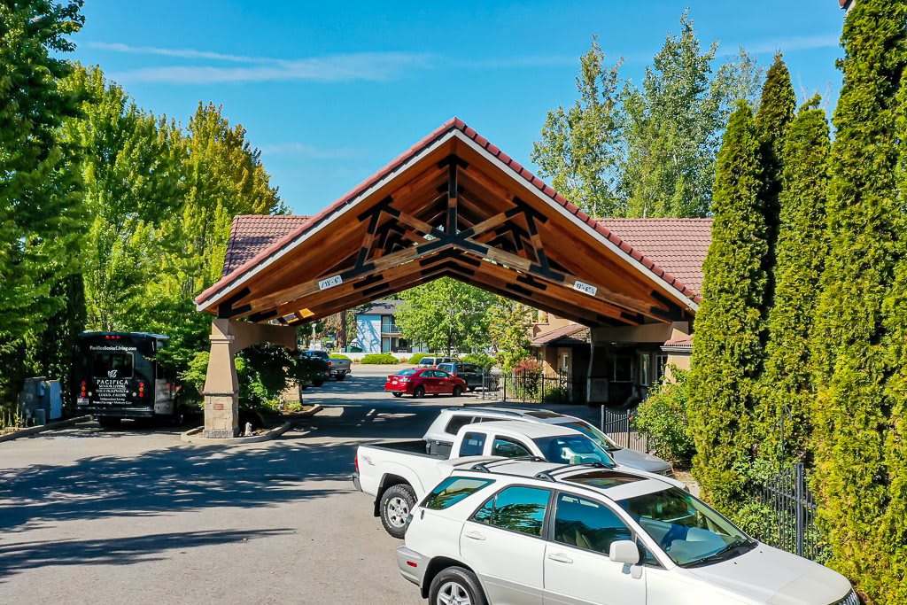 A covered entrance with multiple parked cars and surrounding trees.