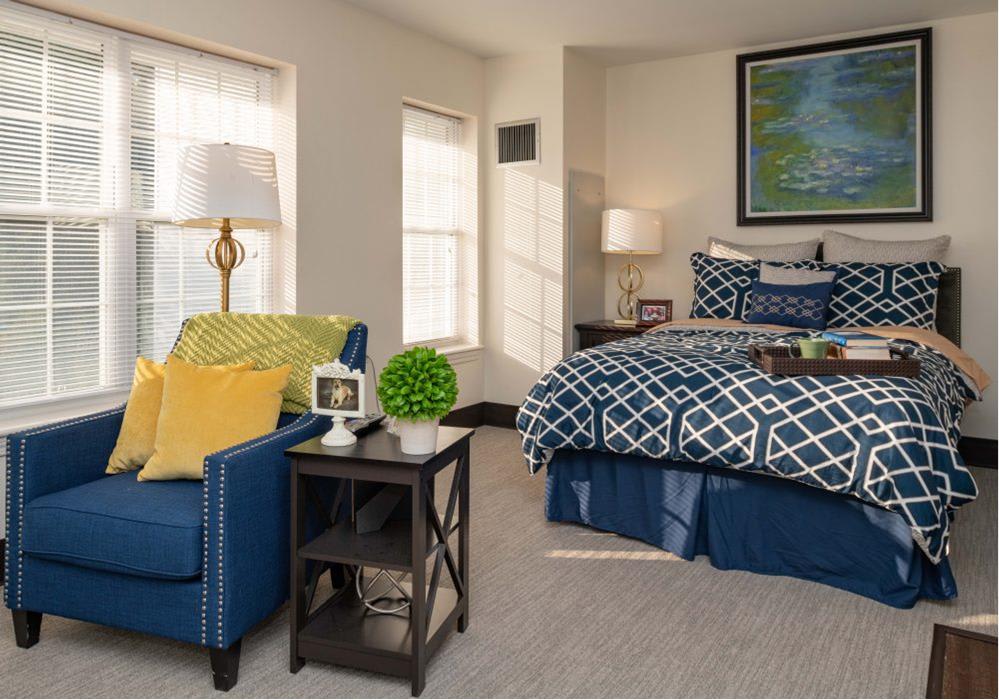 A cozy bedroom with a blue and white patterned bedspread, accompanied by a comfortable blue chair and modern decor.