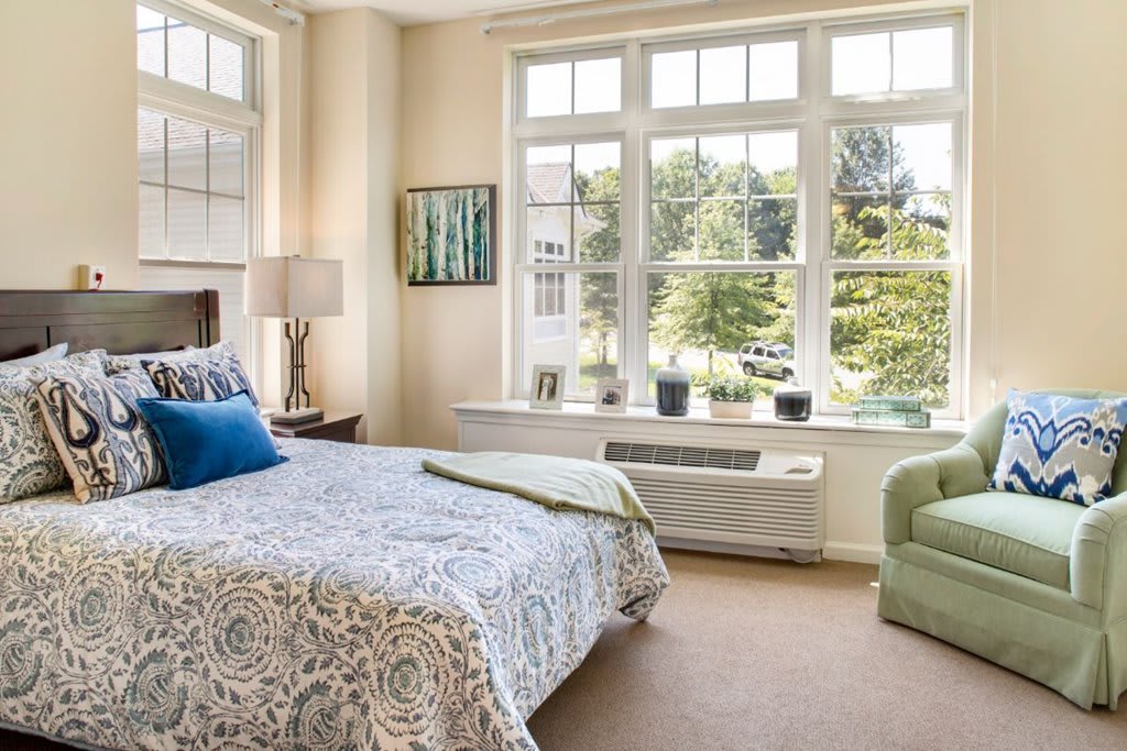 A cozy bedroom featuring a large window, patterned bedding, and comfortable seating.