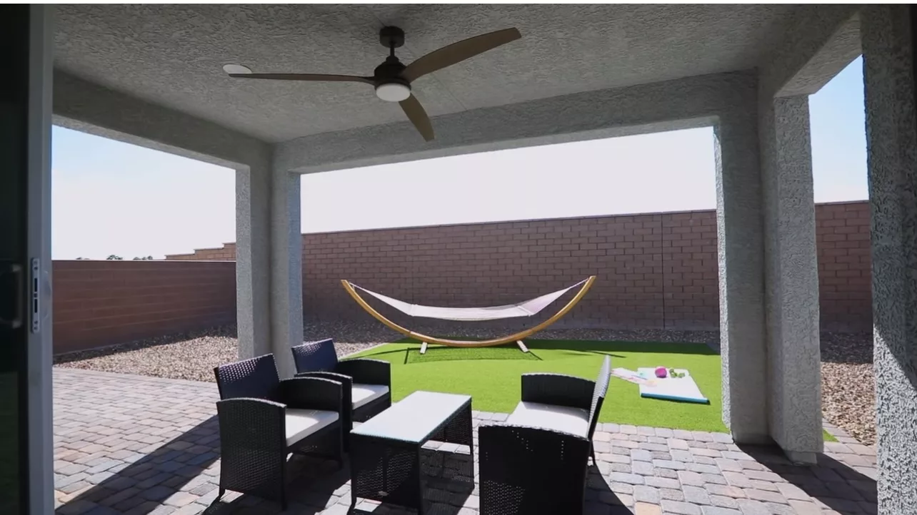 A cozy outdoor patio with modern furniture, a ceiling fan, and a hammock in the backyard.