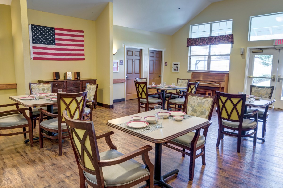 A cozy dining room with neatly arranged tables and chairs, featuring an American flag on the wall.