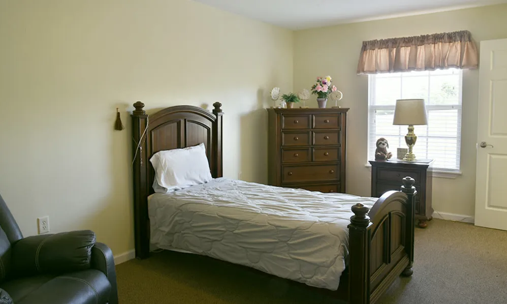 A cozy bedroom with a single bed and a wooden dresser, featuring a window for natural light.