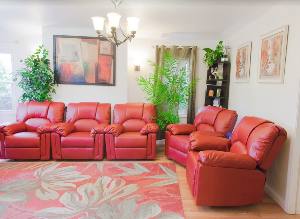 A cozy living room with red sofas, a decorative chandelier, and indoor plants.