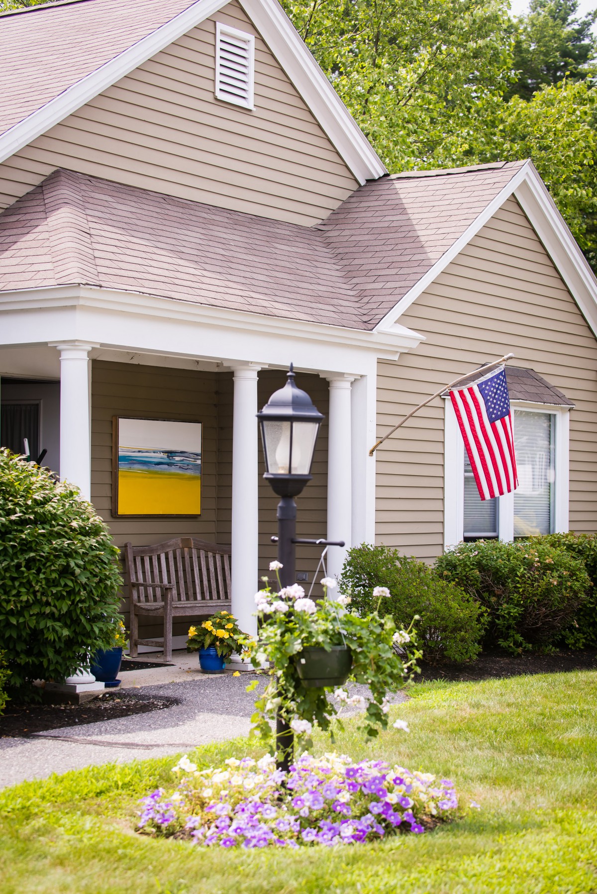 A cozy house with a front porch decorated with an American flag and surrounded by well-maintained landscaping.