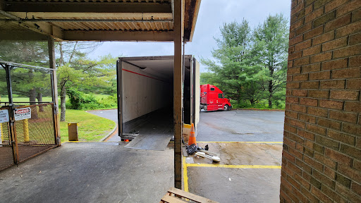 A red truck parked next to an empty trailer at a loading dock surrounded by trees.