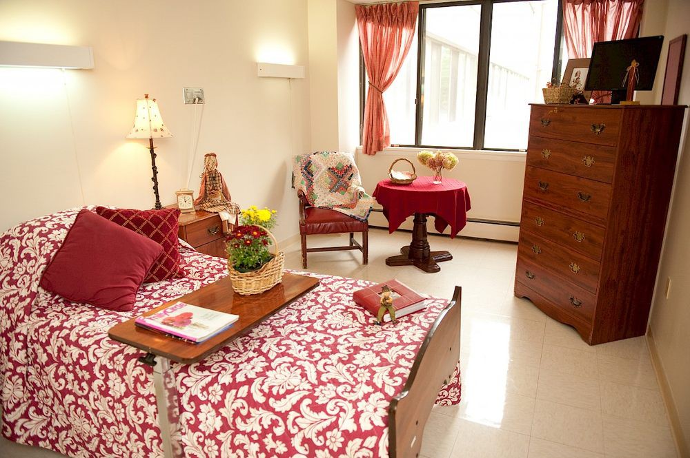 A cozy bedroom with elegant red and white decor, featuring a comfortable bed, dresser, and a small round table by the window.