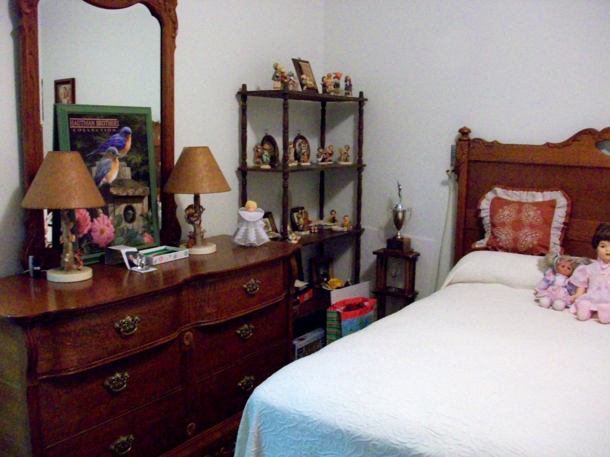 A cozy bedroom with a wooden dresser and mirror, adorned with lamps and decorative items, alongside a neatly made bed.