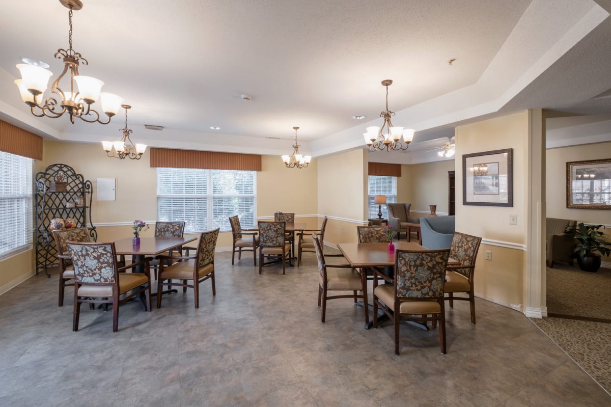 A spacious dining room with multiple tables and chairs, adorned with chandeliers and large windows.