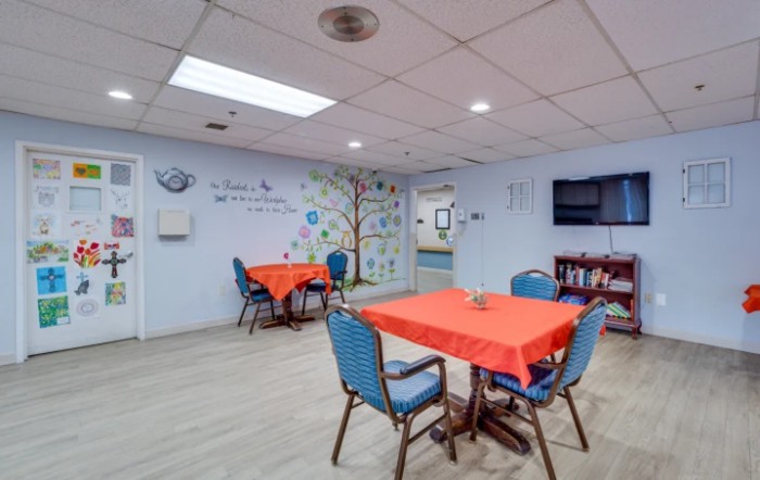 A brightly lit communal dining area with tables covered in red cloths and a decorated wall.
