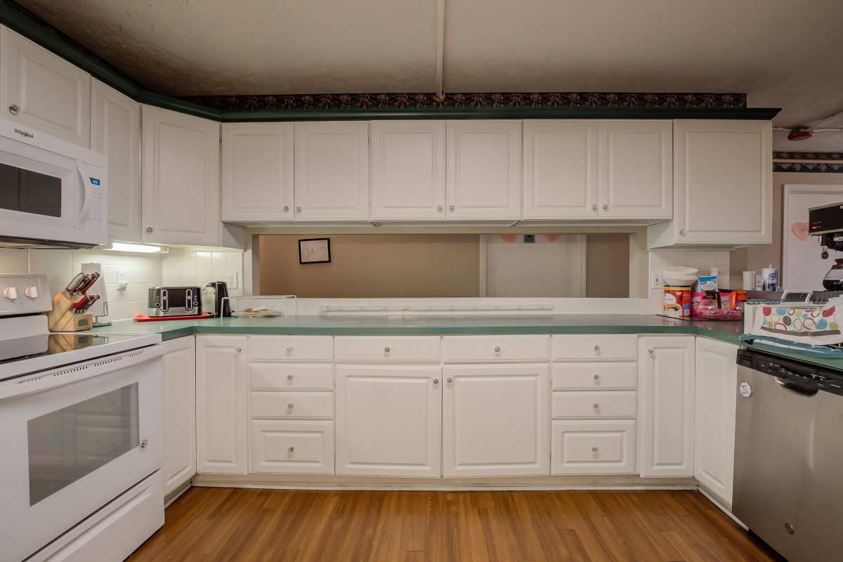 A spacious kitchen with white cabinets and a green countertop, featuring wood flooring and various appliances.