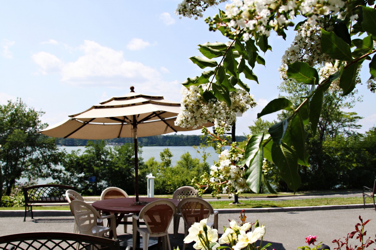 A serene outdoor patio with a view of the lake, featuring chairs and an umbrella under a clear summer sky.