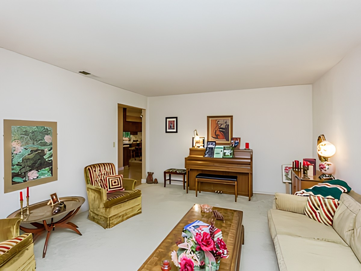 A retro-style living room featuring a piano, armchair, sofa, and coffee table with floral decor.