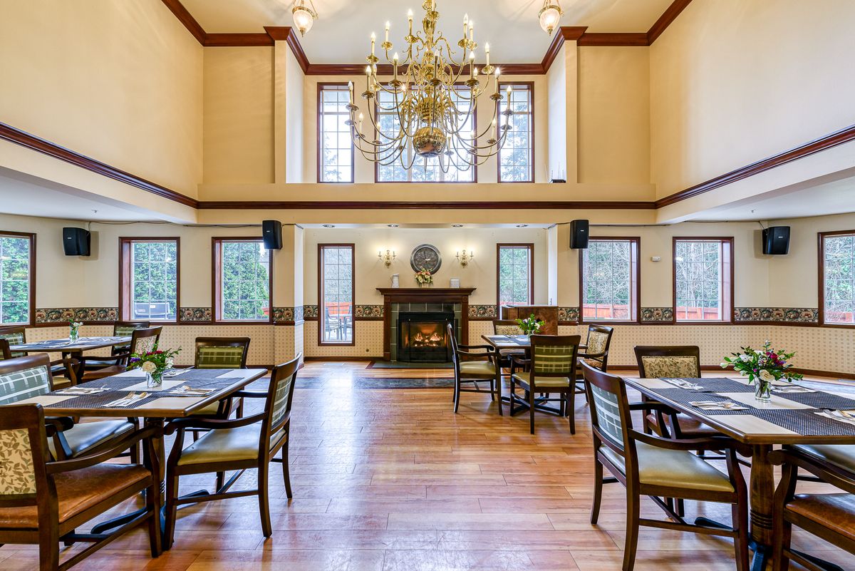 A spacious dining room with elegant decor, featuring a chandelier, fireplace, and multiple tables with chairs.