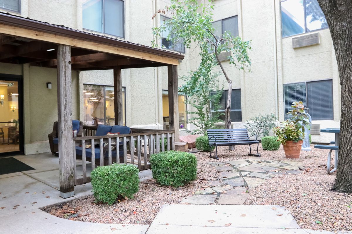 A peaceful courtyard with a covered seating area, surrounded by plants and a stone pathway.