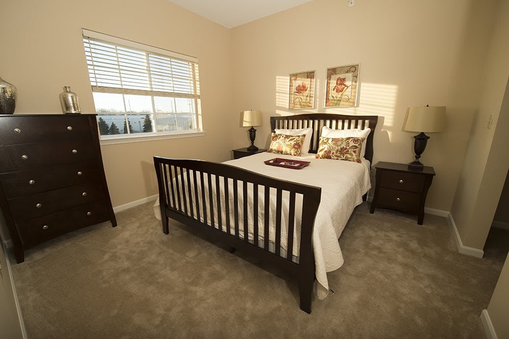 A cozy bedroom with a neatly made bed, side tables, lamps, and decorative artwork.
