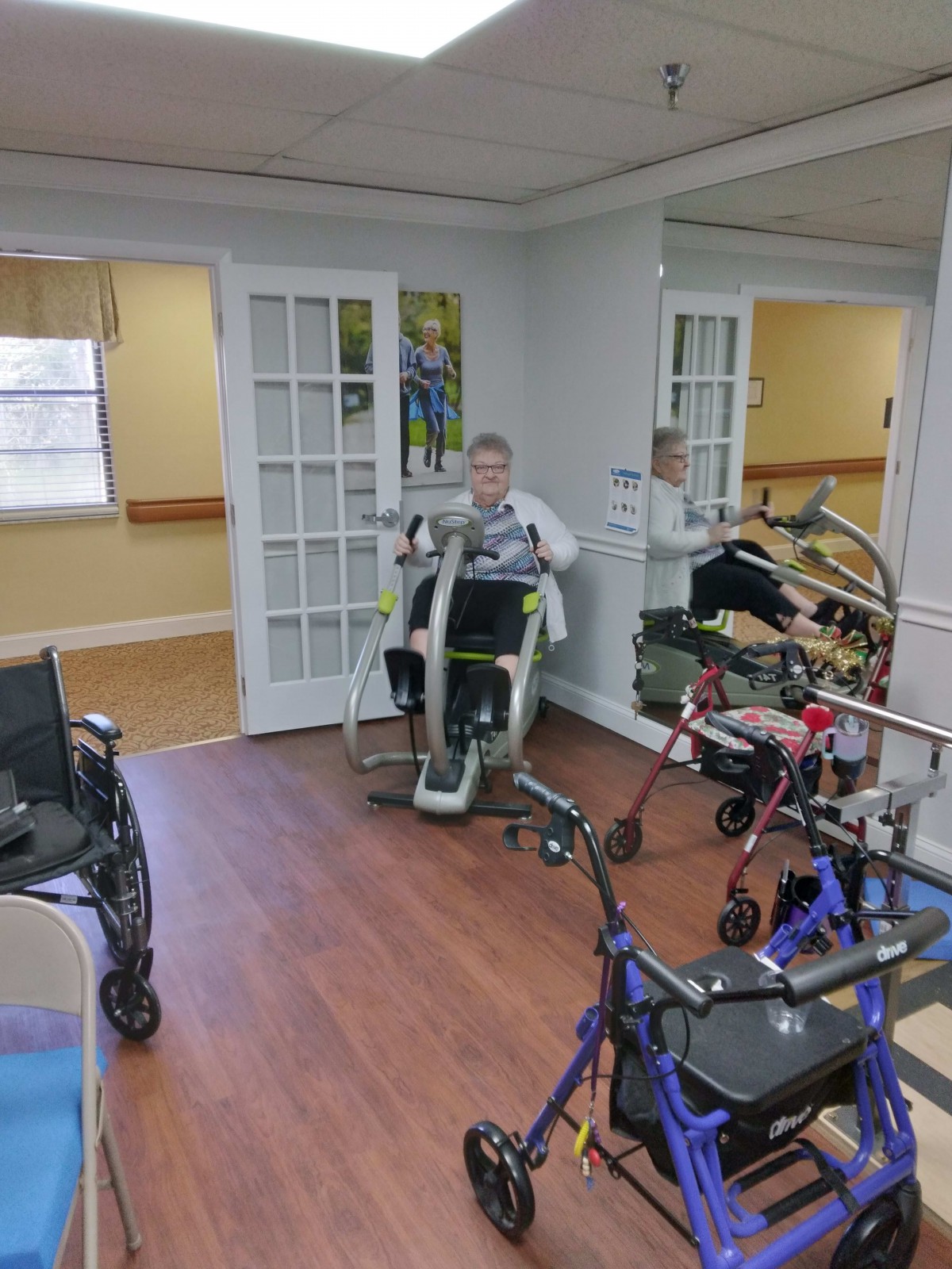 An individual using fitness equipment in a rehabilitation center, surrounded by walkers and mirrors.
