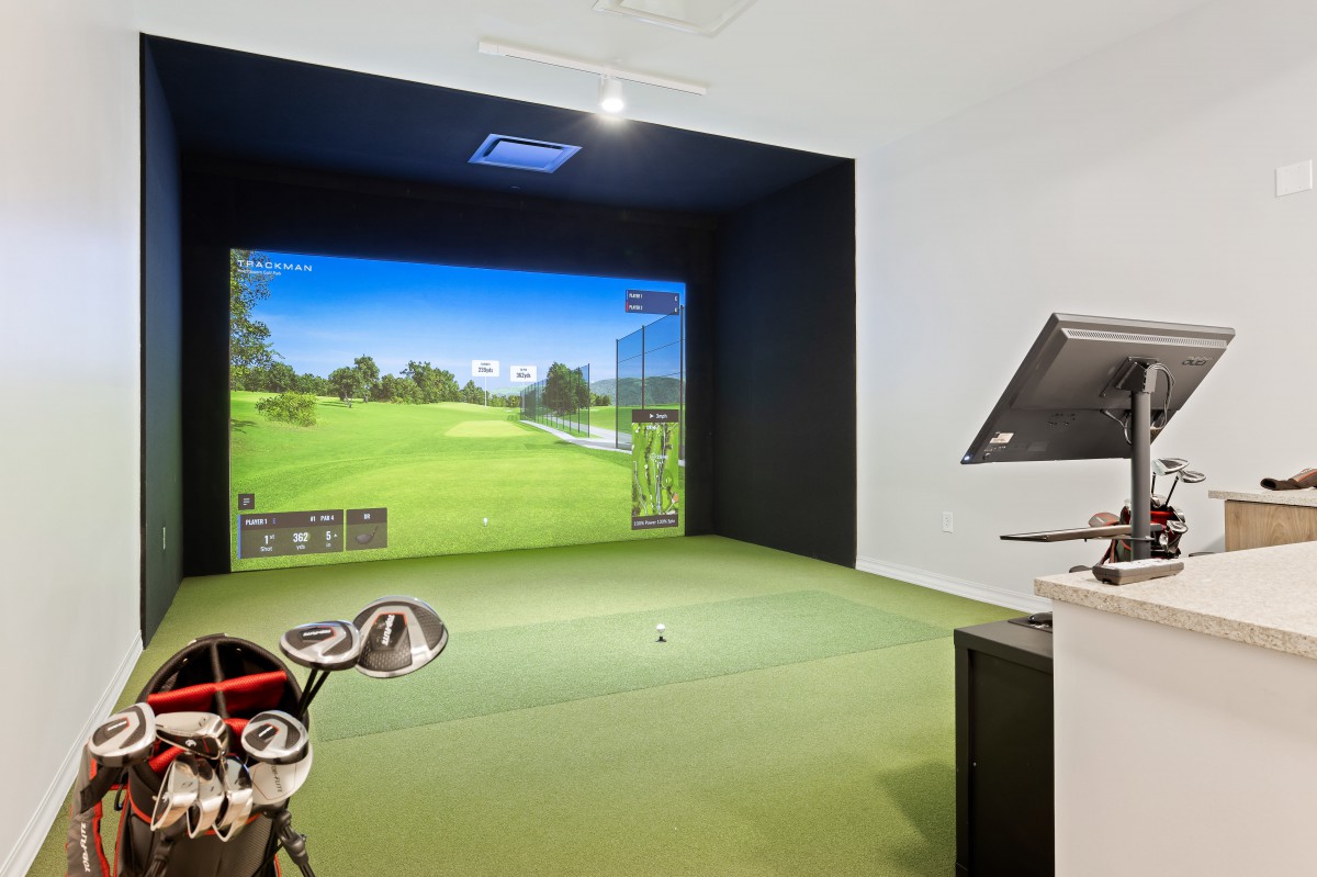 A modern indoor golf simulator setup with a virtual gameplay screen and clubs.