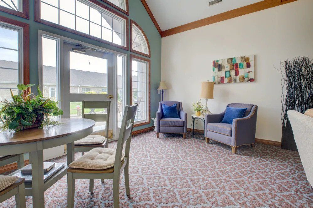 A cozy living room with large windows, featuring two armchairs and a small table.