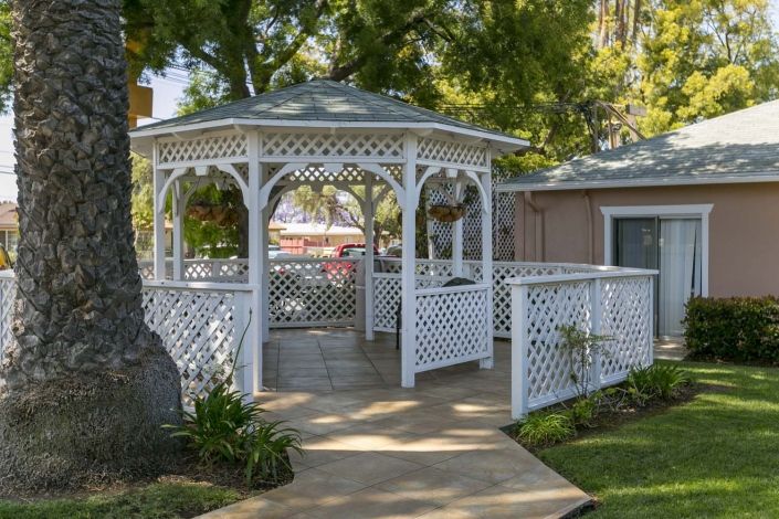 A charming white gazebo with lattice design nestled in a garden setting.