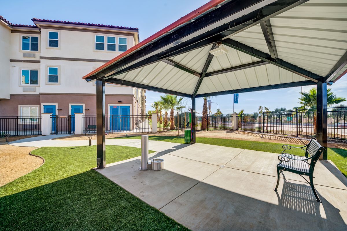 A sunny outdoor area with a gazebo, surrounded by grass and adjacent to a building.