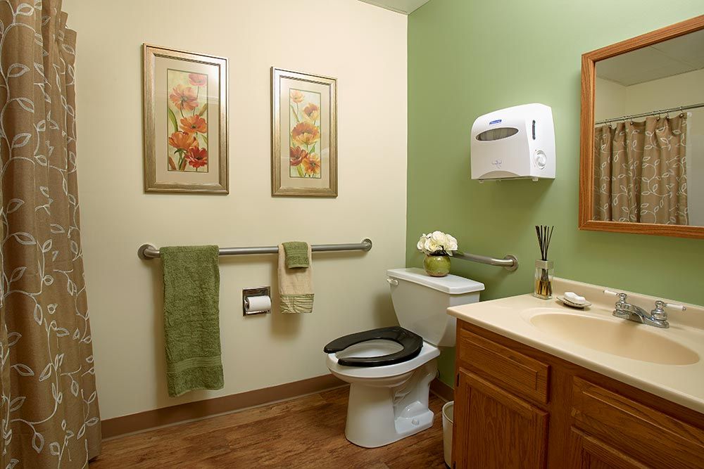 A clean and neatly arranged bathroom with green walls, decorated with floral artwork and equipped with essential amenities.