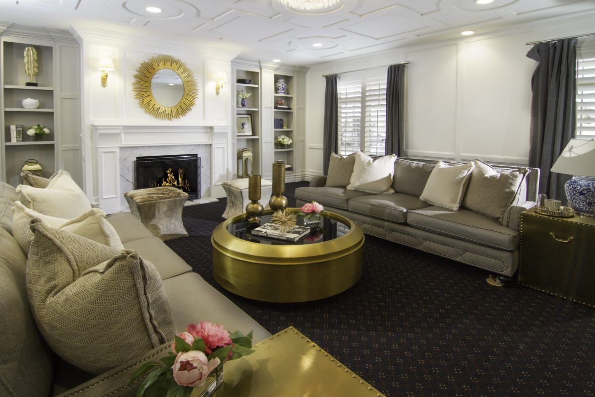 A stylish living room featuring plush sofas, a central round coffee table, and elegant decor including a mirror and fireplace.