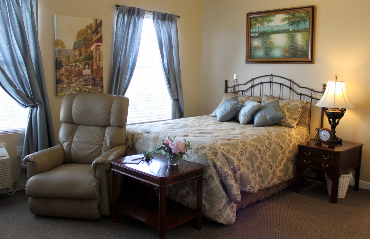 A cozy bedroom with a bed, recliner, and side table under soft lighting.