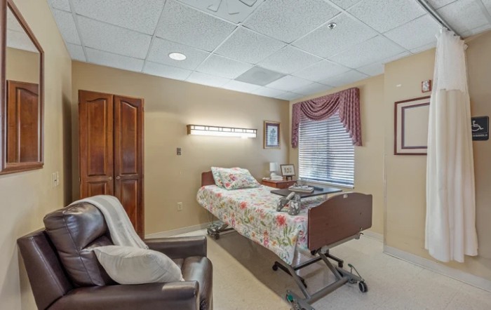 A cozy hospital room with a bed, comfortable chair, and window with drapes.