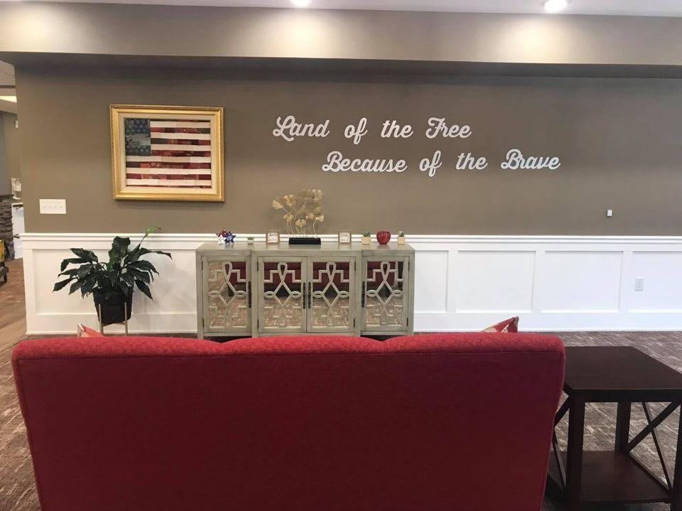 A memorial space featuring an American flag and a patriotic quote on the wall: 'Land of the Free, Because of the Brave.'