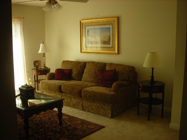 A cozy living room with a sofa, lamps, and a framed painting on the wall.