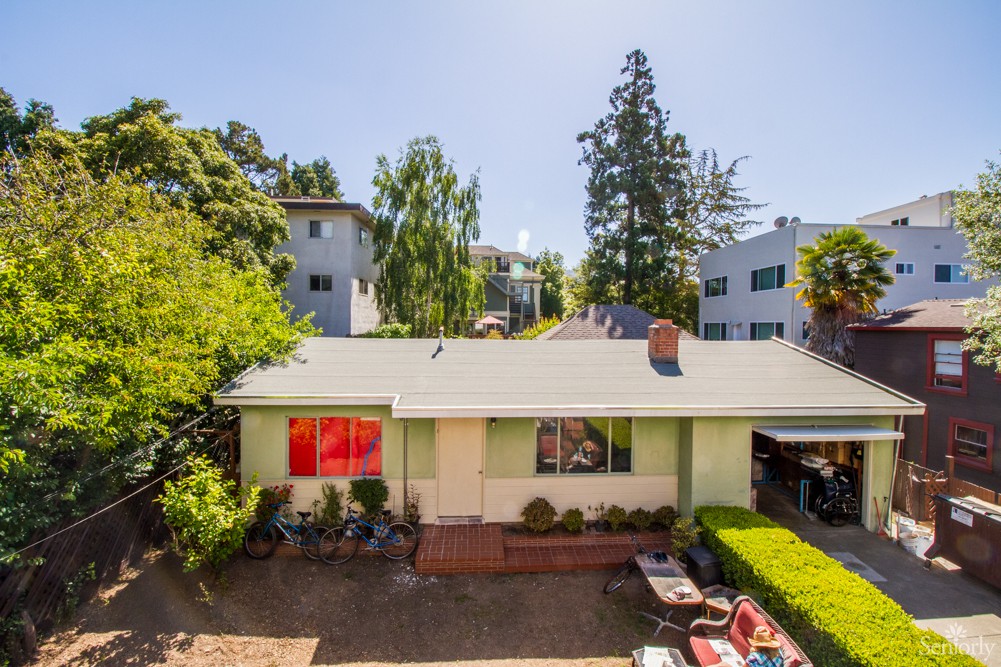 A suburban house with a yard, surrounded by trees under a sunny sky.